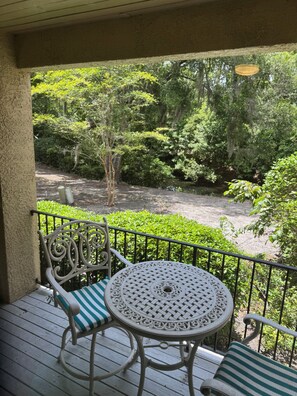 Un balcón con una mesa y sillas, con vistas a un jardín con árboles y un elemento acuático.