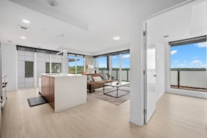 Eine moderne Küche mit Kochinsel, ein Essbereich mit Sofa und Couchtisch sowie große Fenster mit Blick ins Freie.