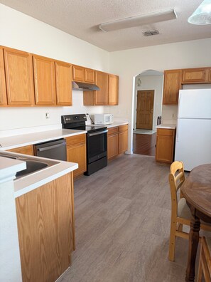 A kitchen with wooden cabinets, a black stove, a white microwave, and a white refrigerator. - Awesome Renovated 3-bedroom house near Dallas Stadium (Euless)