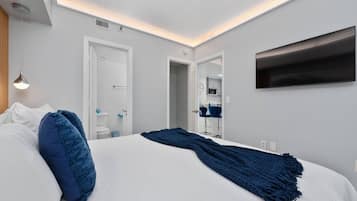 A modern hotel room with a large bed, a flat-screen TV mounted on the wall, and a ceiling light fixture.