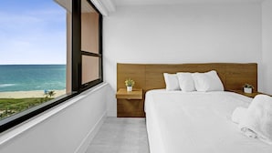 A bedroom with a large window, a wooden headboard, a bed with white bedding, and a small bedside table with a plant. - Stylish Ocean View Retreat Steps from the Beach with Resort Amenities 1508 (Miami Beach)