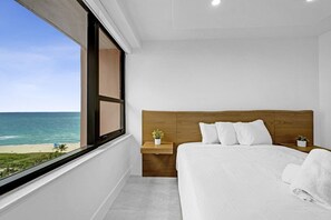 A bedroom with a large window, a wooden headboard, a bed with white bedding, and a small bedside table with a plant. - Stylish Ocean View Retreat Steps from the Beach with Resort Amenities 1508 (Miami Beach)