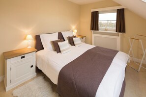 A bedroom with a bed, nightstands, a window with curtains, and a radiator. - Vrbo Property (Middelkerke)