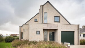 A modern two-story house with a brick exterior, a green garage door, and a front door with a glass panel. - Delmaro, vacation home 6 pers., near beach. (Middelkerke)