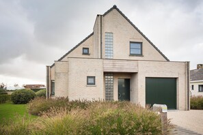 A modern two-story house with a brick exterior, a green garage door, and a front door with a glass panel. - Vrbo Property (Middelkerke)