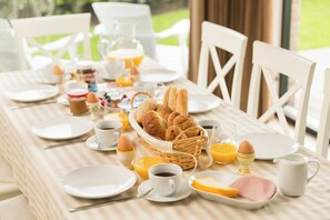 Ein Frühstückstisch ist gedeckt mit Tellern, Tassen, einem Brötchenkorb, Eiern und Orangensaft.