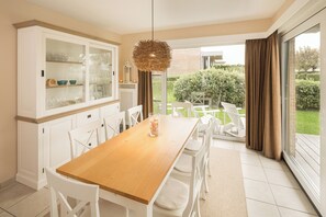 A dining area with a wooden table, white chairs, a glass cabinet, and a view of the outdoors. - Vrbo Property (Middelkerke)