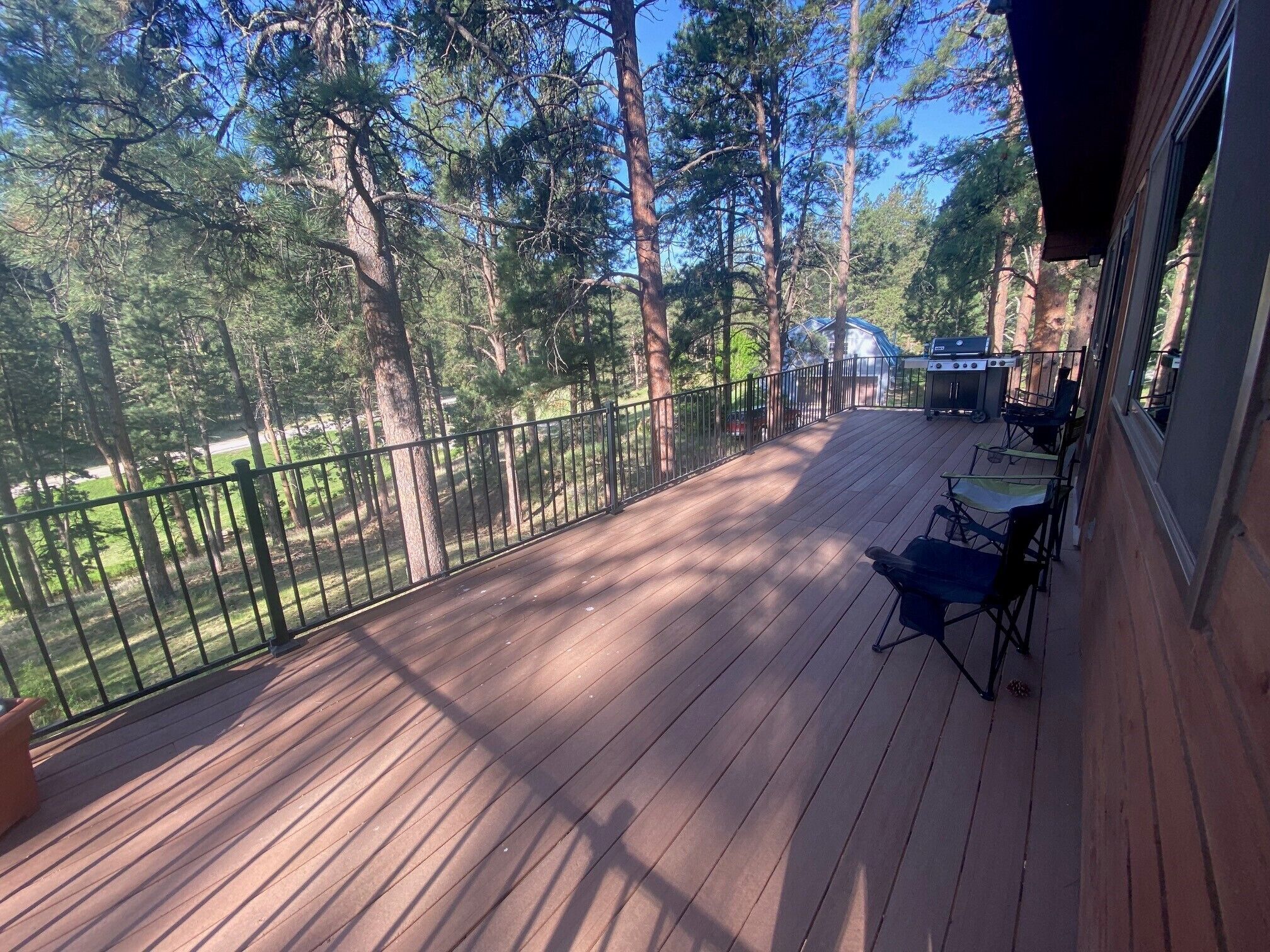 A wooden deck with a metal railing, outdoor furniture, and a view of a forested area.