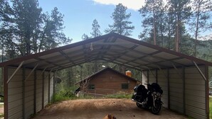 A covered outdoor area with a dirt ground, a dog, and a motorcycle parked under a metal roof. - Gorgeous house for rent during Sturgis Rally 2026 (Rapid City)
