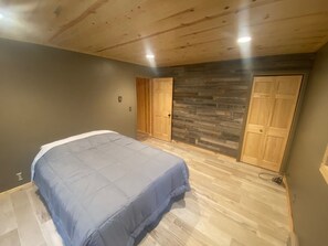 A bedroom with a bed, wooden flooring, a stone wall, and two doors. - Gorgeous house for rent during Sturgis Rally 2026 (Rapid City)