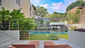 Un espace extérieur moderne doté d’une piscine, de chaises longues en bois et d’un escalier menant à une structure couverte.