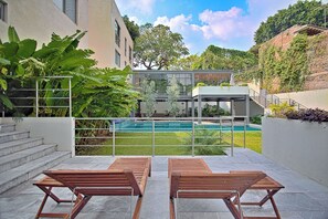A modern outdoor area with a pool, wooden lounge chairs, and a staircase leading to a covered structure. - Black & White Apartment, an oasis in Cuernavaca (Cuernavaca)