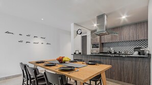Une cuisine moderne avec une table en bois dressée pour le repas, une horloge au mur et un îlot de cuisine équipé d’appareils électroménagers.