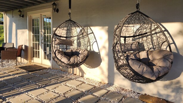 Un patio con dos sillones colgantes tipo huevo, una puerta y una zona de estar con sillas.