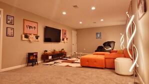 Una sala de estar con un televisor de pantalla plana grande, un sofá modular, una mesa de centro y una alfombra.
