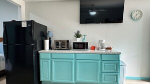 Una cucina con un frigorifero nero, un forno a microonde, un tostapane, una macchina per il caffè e una sveglia appesa al muro.