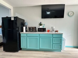 A kitchen with a black refrigerator, a microwave, a toaster, a coffee maker, and a clock on the wall. - Hidden Oasis Bunkhouse (Port O'Connor)