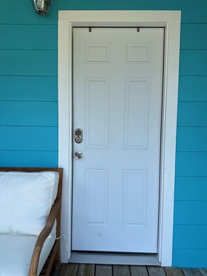 A white door with a keyhole and a small window, set in a teal-painted wall. - Hidden Oasis Bunkhouse (Port O'Connor)