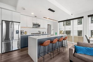 A modern kitchen with a central island, stainless steel appliances, and a bar area with stools. - 2BR | UG Park | AC | Mins to Saddledome (Calgary)
