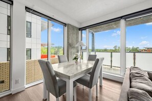 A modern dining area with a table and chairs, large windows, and a balcony with a view. - 2BR | UG Park | AC | Mins to Saddledome (Calgary)