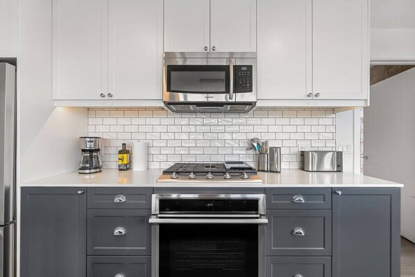 Una cocina moderna con armarios blancos, un microondas de acero inoxidable, una estufa a gas y un horno empotrado.
