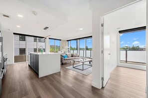 A spacious apartment with a kitchen, living area, and large windows offering views of the outdoors. - 2BR | UG Park | AC | Mins to Saddledome (Calgary)