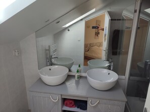Uma casa de banho moderna com duas grandes pias brancas, um espelho e área de duche.