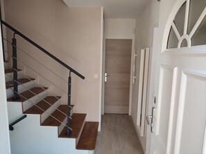 Uma escada com corrimão de metal, degraus de madeira e uma porta com janela de vidro jateado.