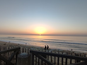 A beach scene with a sunset, waves, and people walking along the shore. - Vrbo Property (Lacanau)