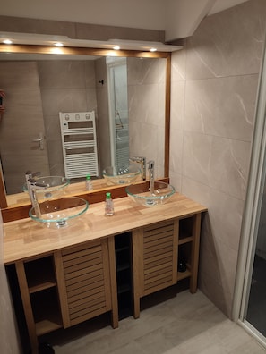 A bathroom with a wooden vanity, two glass bowl sinks, a mirror, and a towel rack. - Vrbo Property (Lacanau)