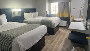 Ett hotellrum med tre sängar, ett skrivbord, en stol och ett fönster med gardiner.