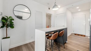 Una cocina moderna con una isla central, taburetes de bar, un espejo redondo y una planta en maceta.