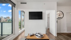 Una sala de estar moderna con un gran ventanal, un televisor de pantalla plana en la pared, una mesa de centro de madera y vistas a la ciudad.