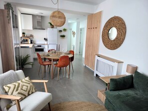 A modern living room with a green sofa, a white armchair, and a dining area with a round table and chairs.