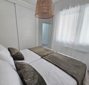 A bedroom with a bed, pillows, a hanging light fixture, and a window with curtains.