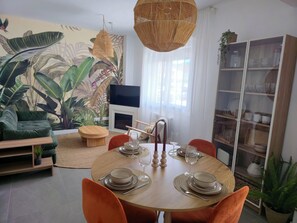 Ein Essbereich mit einem runden Tisch für vier Personen, umgeben von orangefarbenen Stühlen, einem Fernseher und einem Bücherregal.