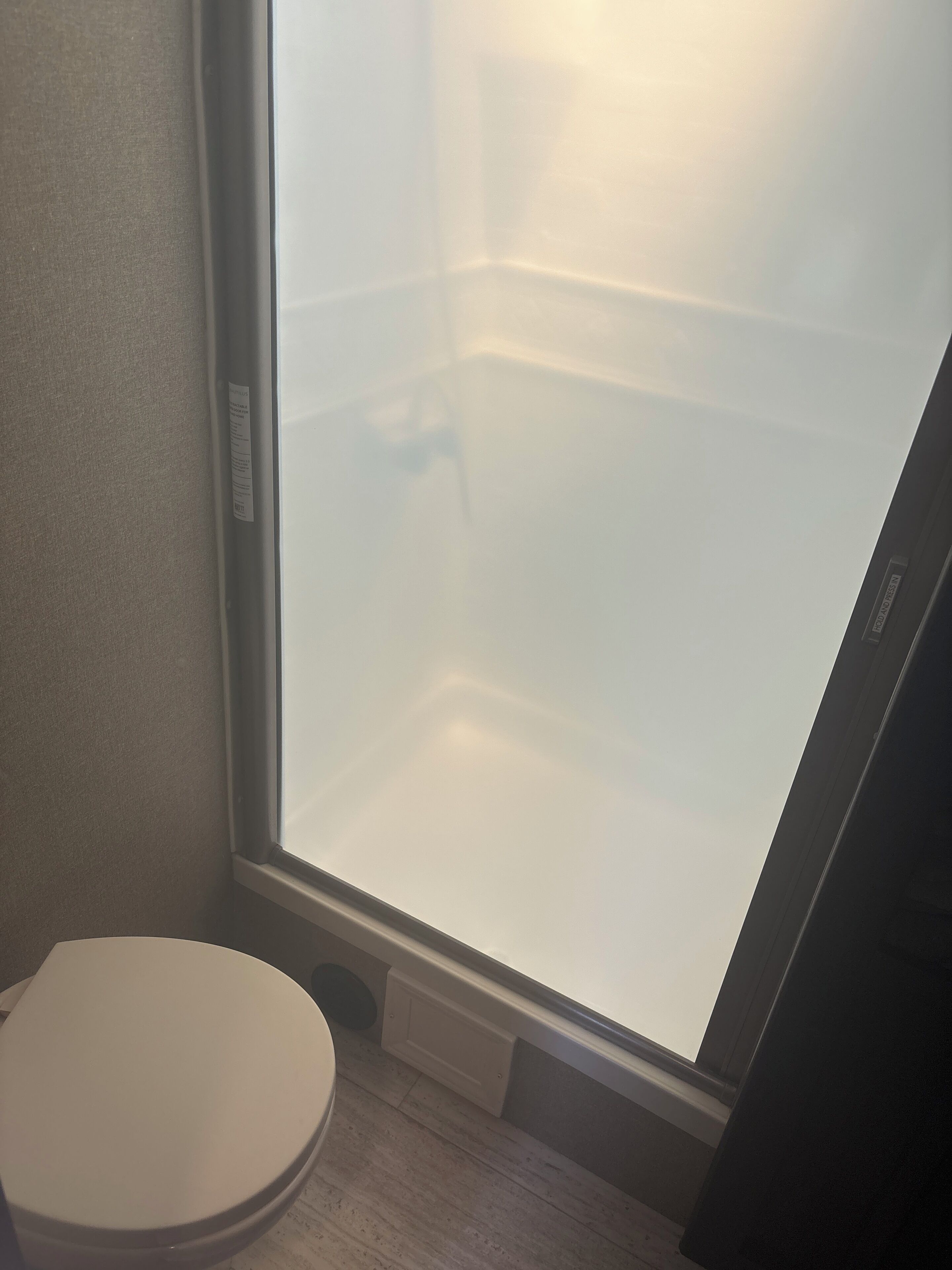 A bathroom with a toilet, a mirror, and a frosted glass door.