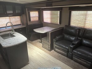 A compact RV interior with a kitchenette, a dining area, and a seating area. - Cozy 1-bedroom Camper on the lake with AC in adorable Cortland. (Cortland)