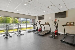 Ein Fitnessstudio mit Laufbändern, Ergometer und einem Fernseher an der Wand.