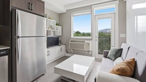 Une cuisine moderne dotée d’un réfrigérateur encastré, un coin repas avec une table blanche et un balcon offrant une vue agréable.