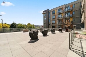 Eine Dachterrasse mit überdachten Grillanlagen, einer Glasumlaufung und einem mehrstöckigen Gebäude im Hintergrund.