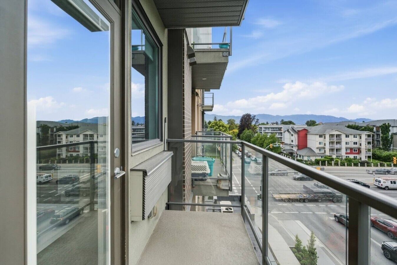 Uma varanda com vista para uma estrada e edifícios, uma porta de vidro e guarda-corrimão de metal.