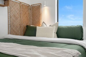 Ein Bett mit grüner Bettwäsche, einer weißen Tagesdecke und Blick zum Himmel durch ein Fenster.