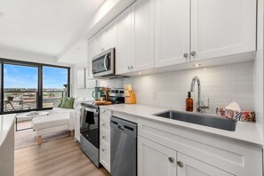 A modern kitchen with white cabinetry, stainless steel appliances, and a large window offering a city view. - NEW | Mins to Saddledome | Rooftop Patio | UG Park (Calgary)