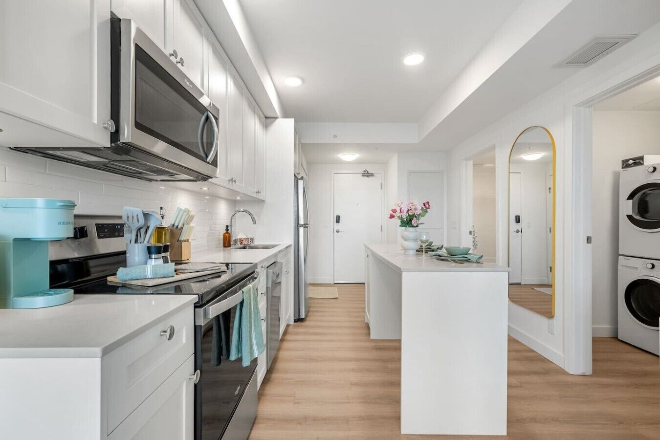 A modern kitchen with a microwave, stove, and coffee maker. There is a central island with a sink and a mirror.
