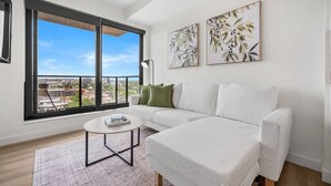 A modern living room with a white sofa, a round coffee table, and two framed botanical prints on the wall. - NEW | Mins to Saddledome | Rooftop Patio | UG Park (Calgary)