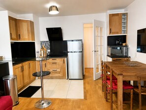Eine kleine Küche mit Kühlschrank, Mikrowelle und Herd, Holzausstattung und einem Essbereich mit Tisch und Stühlen.