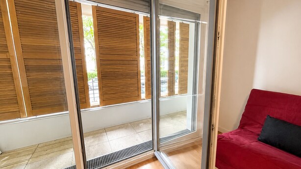 A room with a sliding glass door, a red sofa, and a tiled floor.