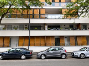 Ein mehrstöckiges Gebäude mit Balkonen, geparkten Autos und einem Baum im Vordergrund.