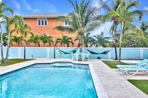 Una piscina con sillas de descanso, palmeras y un edificio al fondo.